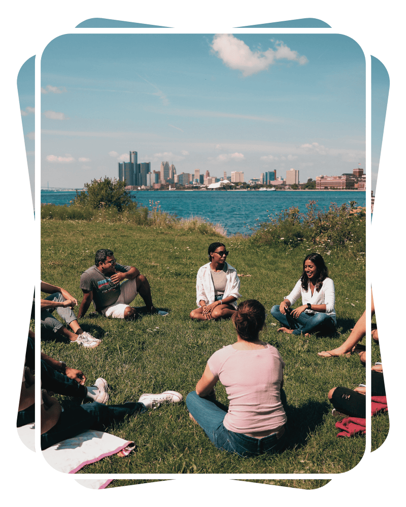 Group Therapy Session in Grass Next to Water with Downtown Detroit in Background